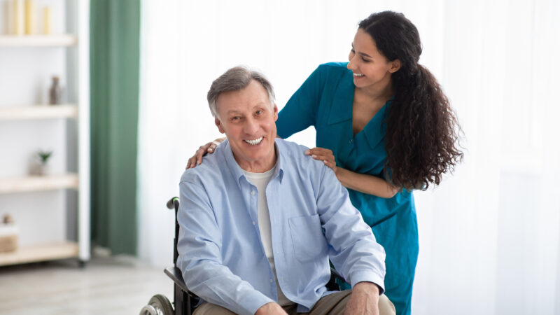 Portrait of happy impaired elderly man and his female nurse at retirement home. Professional medical care for seniors