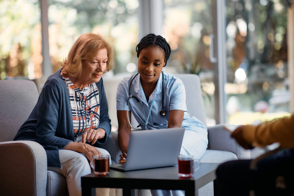 Young black nurse and senior woman using laptop at residential care home.